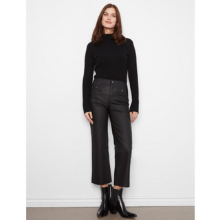 A woman stands against a plain white wall wearing a black ribbed mock-neck long-sleeve top, black cropped wide-leg trousers, and black ankle boots.