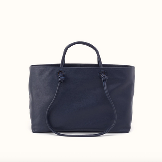 A navy blue pebbled leather tote bag with knotted top handles and a long shoulder strap, photographed against a clean white background.