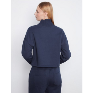 A woman shown from the back wearing a navy blue cropped mock-neck sweater and matching navy pants against a light gray studio background.