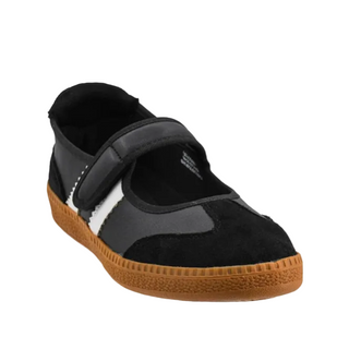 A single Mary Jane style shoe in black suede and black fabric, featuring a white stripe detail and a textured brown gum sole, shown against a plain white background.
