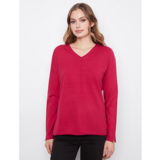 A woman modeling a bright red long-sleeve V-neck knit sweater with black pants, standing against a light gray studio background.