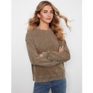 A woman modeling a washed taupe-brown long-sleeve crewneck sweatshirt with distressed details, paired with blue jeans, against a light gray studio background.