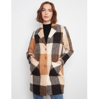 A woman wearing a mid-length plaid coat in beige, brown, black, and cream, layered over a black top and blue jeans, photographed against a light gray studio background.