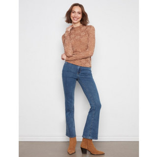 A woman modeling a brown textured knit mock-neck top and blue flare jeans with tan ankle boots, standing against a plain white wall.