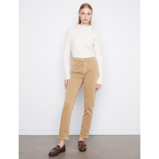 A model stands against a white studio wall wearing a cream ribbed mock-neck long-sleeve top, tan straight-leg pants, and dark brown leather loafers.