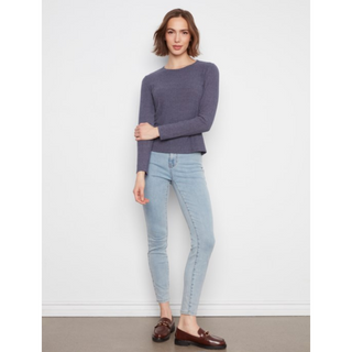 A woman modeling a medium grey long-sleeve knit sweater and light-wash skinny jeans with brown leather loafers, standing against a plain white wall.