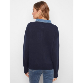 A woman viewed from the back wearing a navy blue knit sweater with a light blue denim collar, paired with blue jeans, against a plain light gray background.