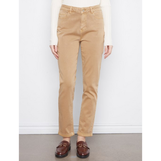 A person wearing straight-leg tan pants with a cream ribbed long-sleeve top and brown loafers, standing against a white wall.