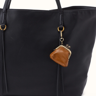 A close-up of a black pebbled leather tote bag featuring a brown leather coin purse charm with gold-tone hardware hanging from the side strap.