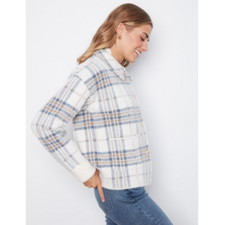 A woman wearing a white plaid knit cardigan with blue and beige stripes, paired with blue jeans, photographed against a light gray studio background.