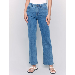 A person wearing medium-wash blue straight-leg jeans with a white top and white slide sandals, standing against a light gray studio background.