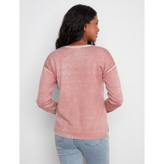 A woman viewed from the back wearing a long-sleeve dusty pink top with white contrast trim at the shoulders and neckline, paired with light blue jeans, against a light gray studio background.
