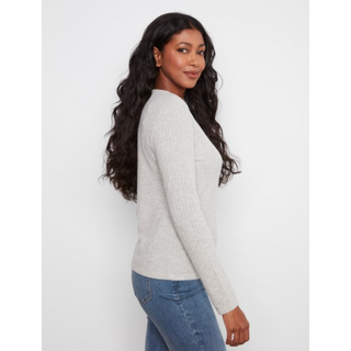 A woman with long, wavy black hair is shown from a side-back angle wearing a light gray ribbed knit sweater and blue jeans against a plain light gray studio background.
