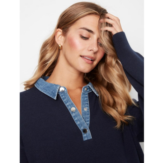 A woman wearing a navy blue knit top with a light blue denim-style collar and button placket, posed against a light gray studio background.