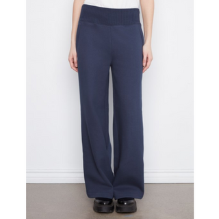 A person wearing navy wide-leg knit pants with a ribbed waistband, paired with a white top and black shoes, standing against a plain white wall.
