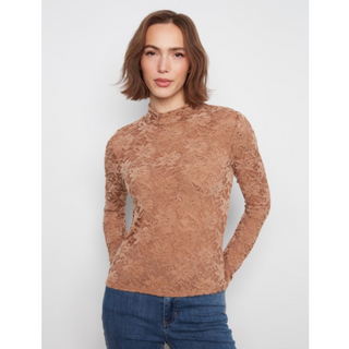 A woman wearing a long-sleeve, high-neck lace top in a warm tan-brown color, paired with blue jeans, against a plain light gray background.